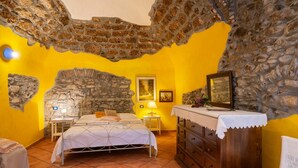 A room with a stone wall, a bed with a white bedspread, a wooden dresser, and a nightstand with a lamp. - Lovely apartment for 3 people with WIFI and balcony (Dolcedo)