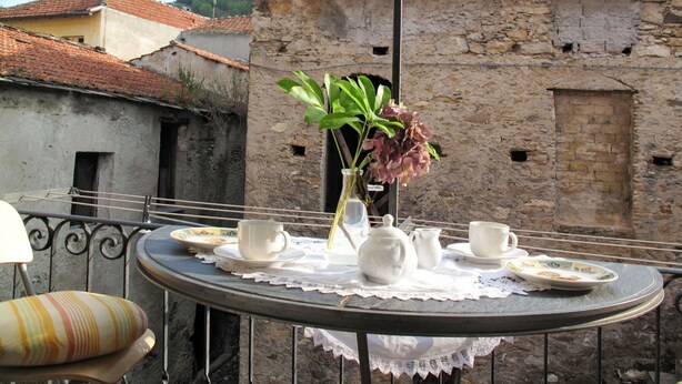 A round table with a lace tablecloth, white teacups, a teapot, and a vase with flowers. - Lovely apartment for 3 people with WIFI and balcony (Dolcedo)
