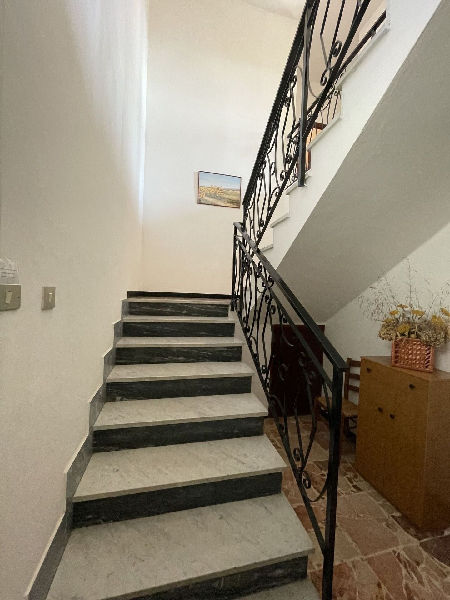 Un escalier avec une rampe en métal noir et un mur en pierre.