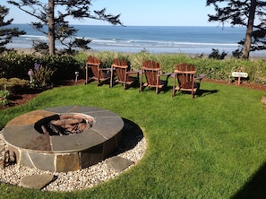 Relax in style with a stone fire pit at the center of this serene outdoor seating area, overlooking a tranquil beach.
