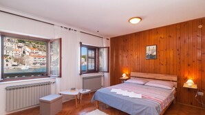 Ein Schlafzimmer mit einem Bett, zwei Nachttischen, einem Fenster mit Blick auf eine Stadt, Holzvertäfelung an den Wänden und einem Heizkörper unter dem Fenster.