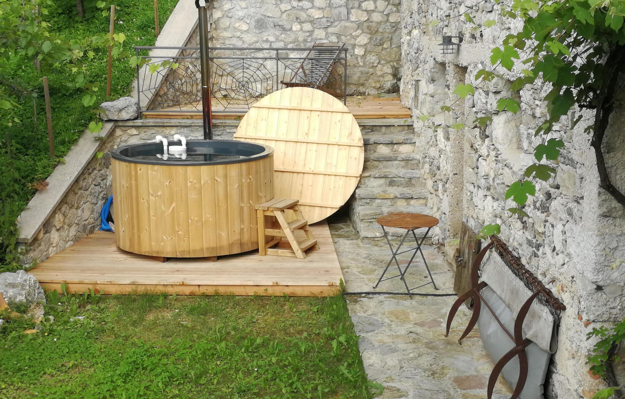 Un bain à remous en bois et une terrasse en bois, le tout intégré dans un décor extérieur rustique agrémenté de murs en pierre.