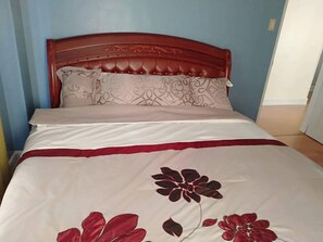 Ein Bett mit einem roten Kopfteil, weißer Bettwäsche und einem Kissen mit Blumenmuster.