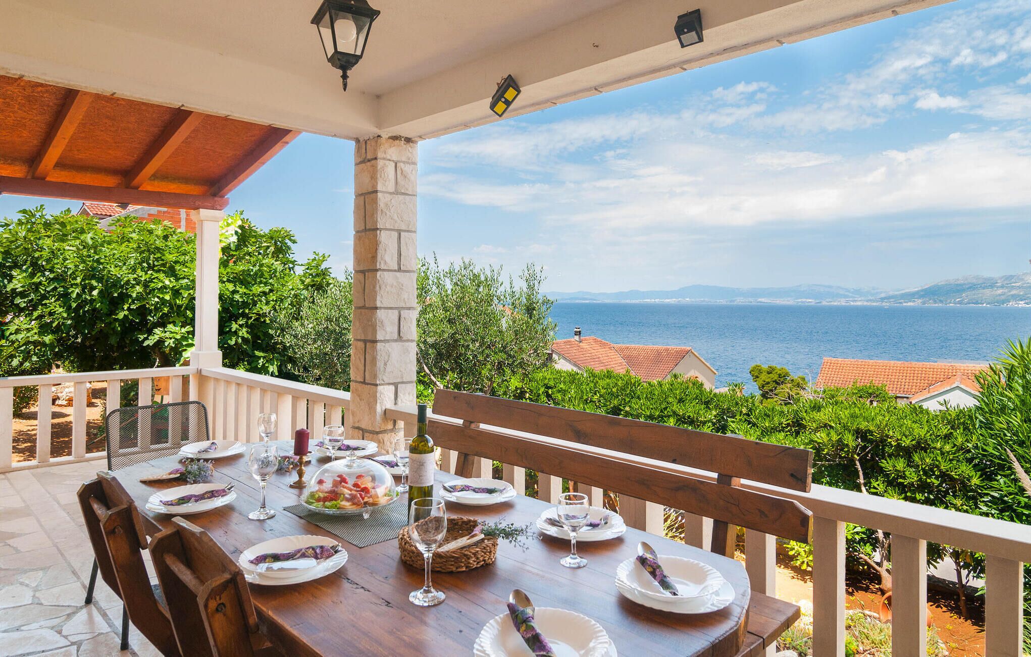 A dining table set outdoors with a view of the sea and mountains.