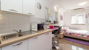 A compact kitchen with a microwave, sink, and cabinets. There is a small dining area with a chair and a bed with a patterned bedspread. - Awesome apartment in Rukavac with WiFi (Rukavac)