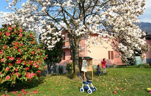 Un jardín con árboles en flor, un cochecito de bebé y un edificio al fondo.