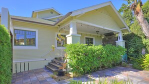 A two-story house with a covered porch, a front door, and a small front yard with a garden and steps leading up to the entrance. - Downtown Craftsman Bungalow (Santa Barbara)