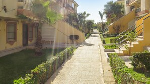 A narrow pathway flanked by buildings with balconies and a small garden area with palm trees and shrubs. - Amazing apartment in Torrevieja with WiFi (Torrevieja)