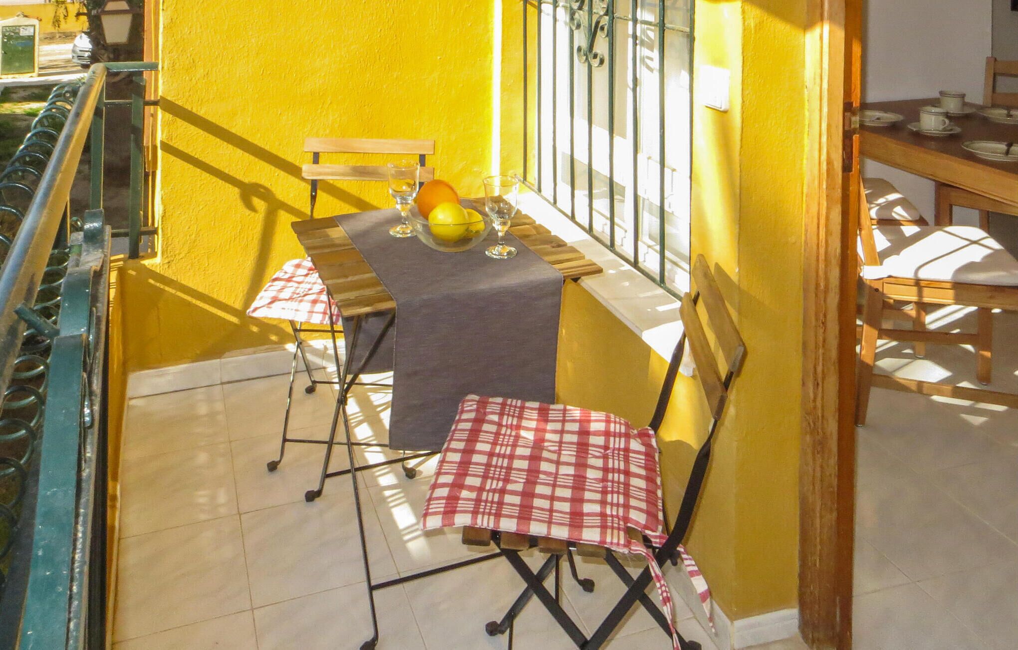 A small outdoor dining area with a table and chairs, a yellow wall, and a view of the street.