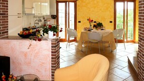 Uma sala de jantar com uma mesa posta para dois, cozinha ao fundo e lareira de tijolos.