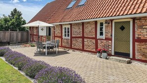 Ett hus byggt av rött tegel med ett tak täckt av takpannor, en uteplats med ett bord och stolar samt en trädgård med lila blommor.