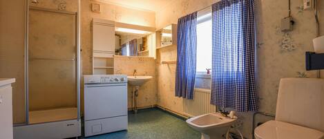 Et lille badeværelse med vaskemaskine, håndvask og toilet.