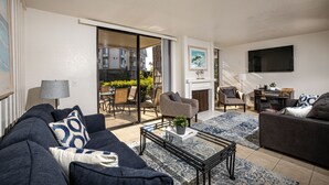 Un salon moderne comprenant un canapé, des fauteuils, une table basse et un téléviseur. Une porte-fenêtre coulissante donne accès à un espace extérieur aménagé avec une table et des chaises.