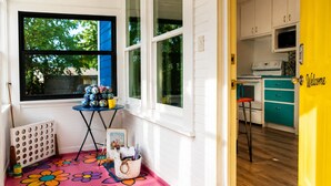 A room with a colorful flower-patterned floor, a table with art supplies, and a kitchen area with teal cabinets and a yellow door.