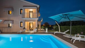 Une maison à deux étages avec une piscine, un espace salon extérieur et un grand parasol.