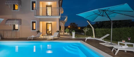 A two-story house with a swimming pool, outdoor seating, and a large umbrella.
