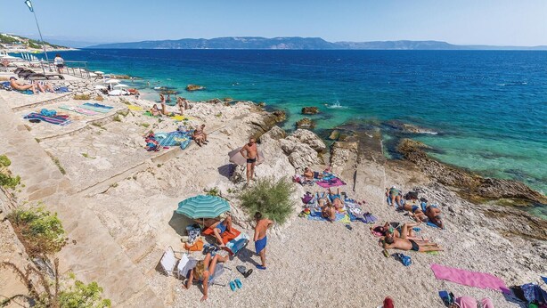 Une plage où l’on peut se détendre au soleil et se baigner, un paysage rocheux et une mer d’un bleu limpide.