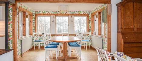 A dining area with a wooden table and chairs, large windows, and a wooden cabinet.