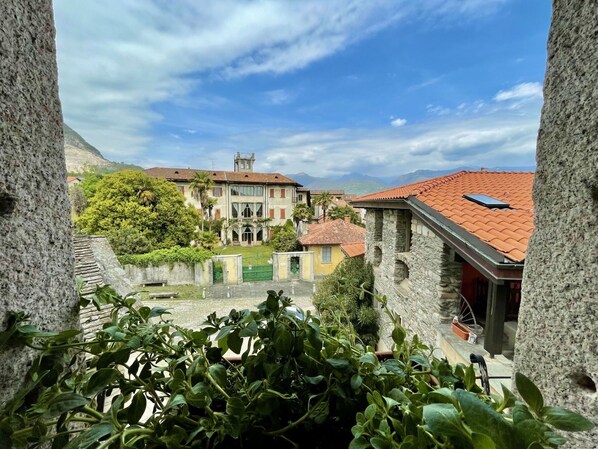 A courtyard with a large building featuring a red-tiled roof, surrounded by greenery and stone walls.