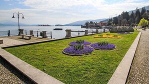 Une promenade en bord de mer, agrémentée de bancs, de parterres de fleurs et offrant une vue dégagée sur le lac et les bâtiments situés au loin.