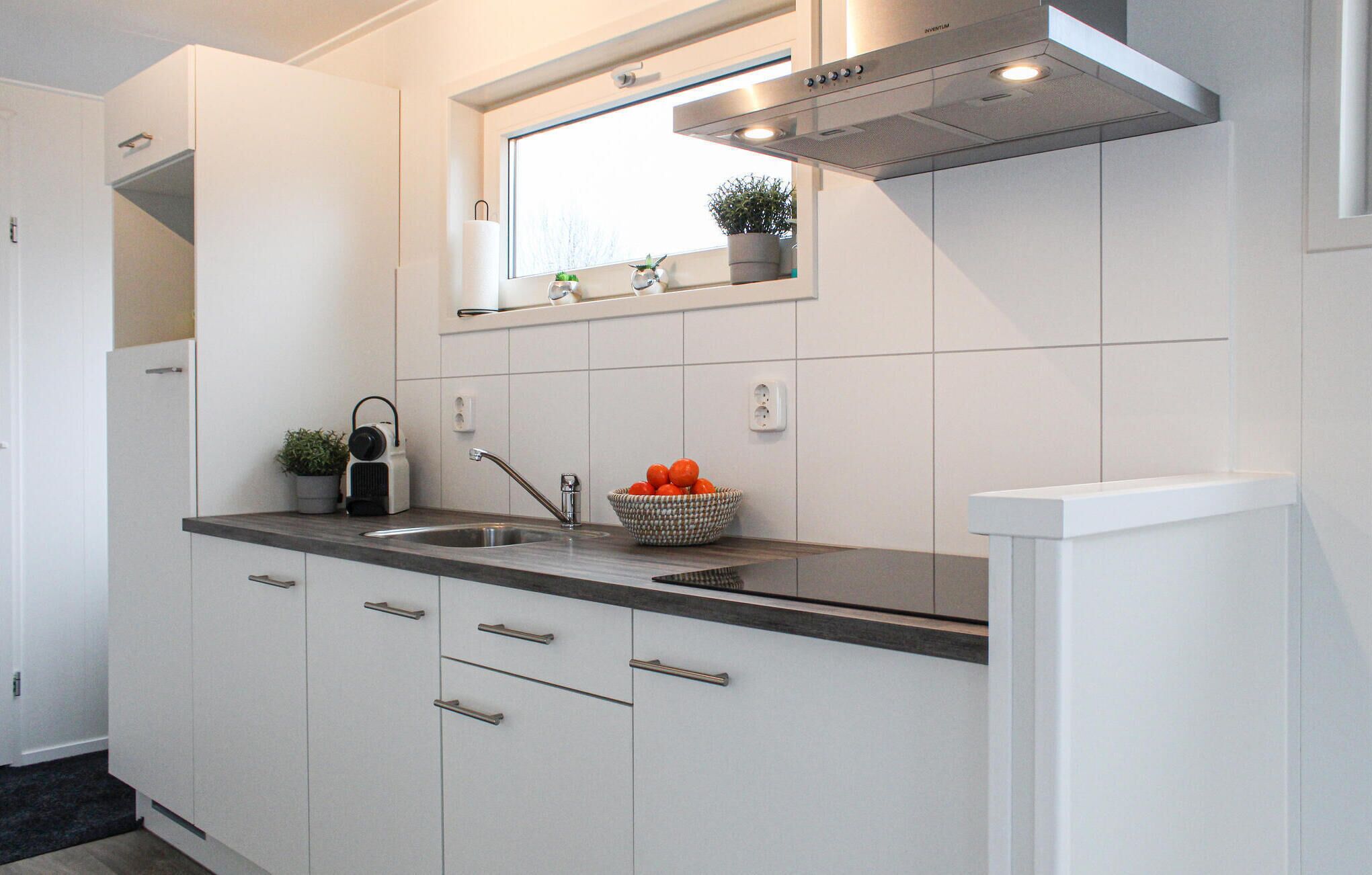 Una cocina moderna con armarios blancos, encimera negra, pileta de acero inoxidable y ventana sobre la pileta.