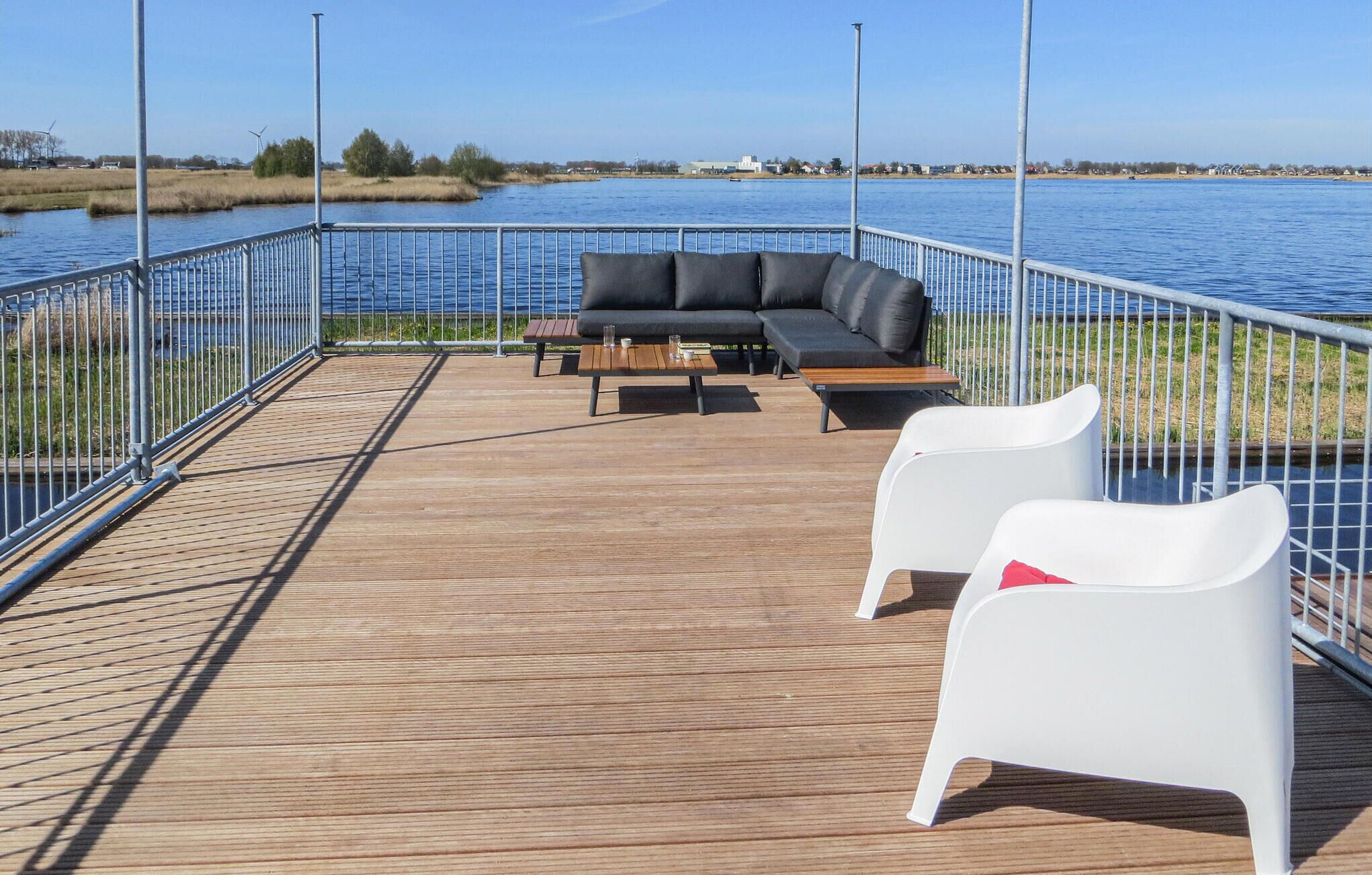 A deck with a black sofa, two white chairs, and a wooden table.