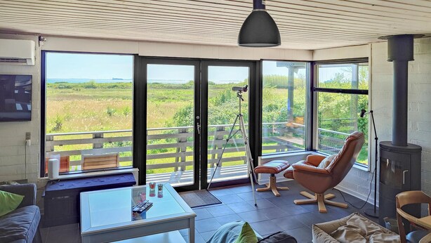 Een moderne woonkamer met een glazen tafel, lederen fauteuils en een groot raam met uitzicht op een groen landschap.