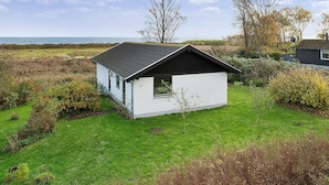 Een klein, wit gebouw met één verdieping en een donker dak, gelegen op een grasveld met uitzicht op zee.