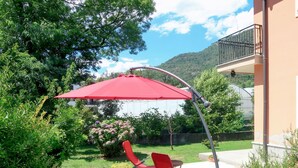 Een terras met een rode parasol, twee rode stoelen en een kas op de achtergrond.
