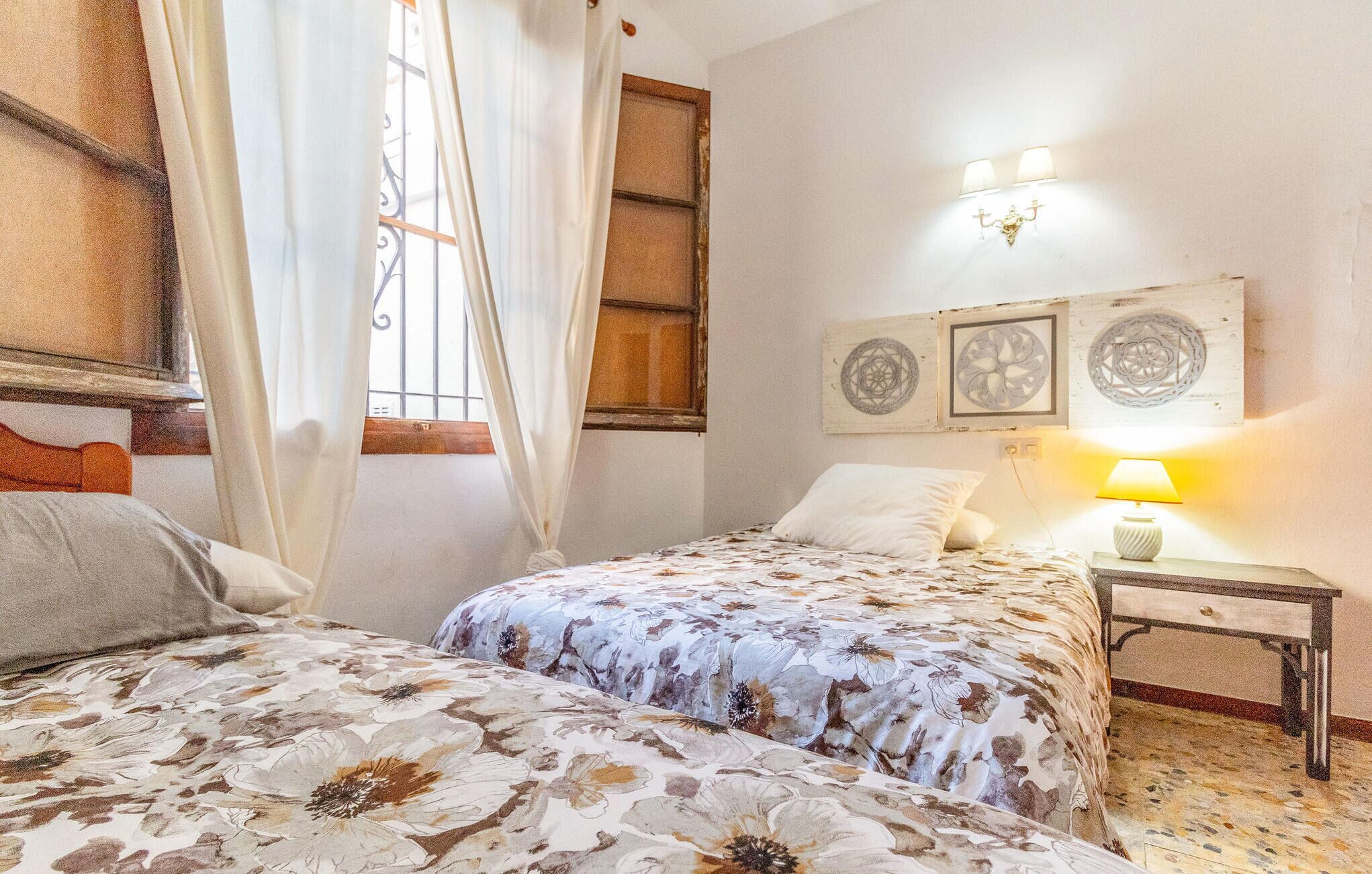 Une chambre avec deux lits, une fenêtre avec des rideaux, une table de chevet avec une lampe et des œuvres d’art murales.