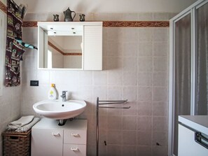 Ein Badezimmer mit einem weißen Waschbecken, einem Spiegel darüber und einem Handtuchhalter. Es gibt einen kleinen Schrank mit Schubladen und einen Korbwannenkorb.