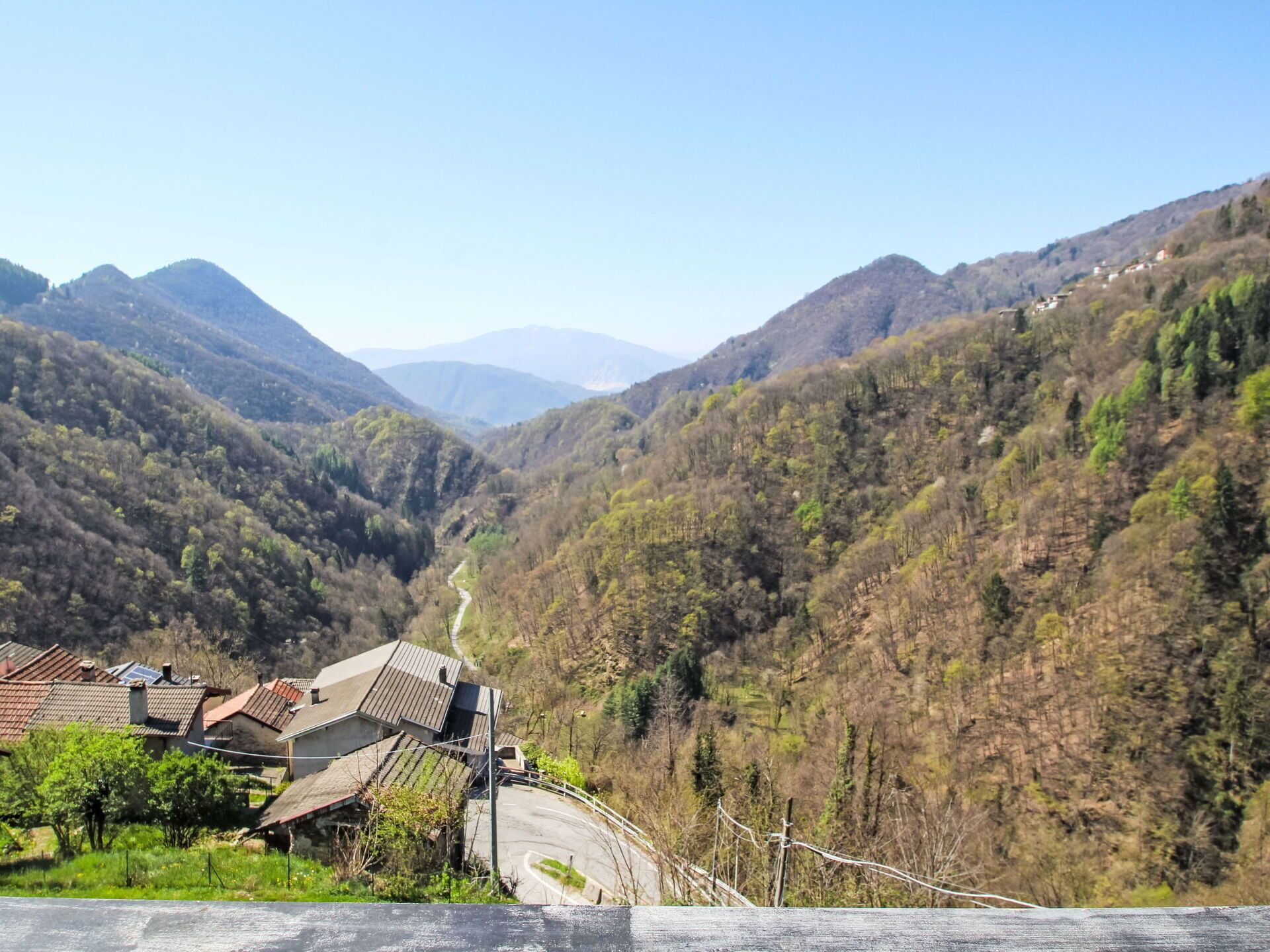 A rural landscape with a winding road, houses with sloped roofs, and dense forested hills.