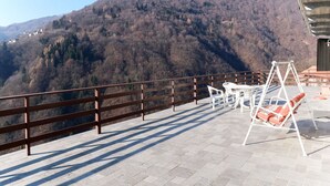 A terrace with a view of a mountainous landscape, a swing chair, and a table with chairs. - Cosy apartment for 4 people with TV, terrace and pets allowed (Aurano)