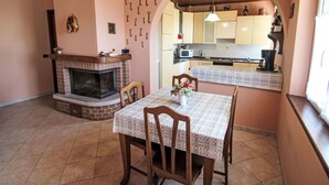 A cozy kitchen with a fireplace, a dining table with chairs, and a kitchen counter. - Cosy apartment for 4 people with TV, terrace and pets allowed (Aurano)