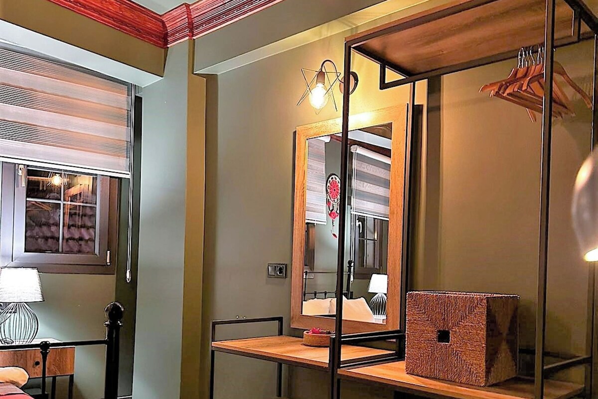 A room with a bed, a desk, a chair, a mirror, and a hanging light fixture.