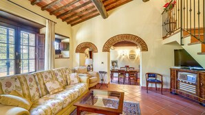 A spacious living room with a sofa, coffee table, and a dining area with chairs and a table. There is a staircase with a railing and a TV stand with a radio. - Gorgeous home in Monte San Savino with WiFi (Monte San Savino)