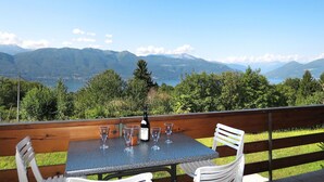 Une table avec quatre verres à vin et une bouteille, placée sur un balcon donnant sur un paysage montagneux.