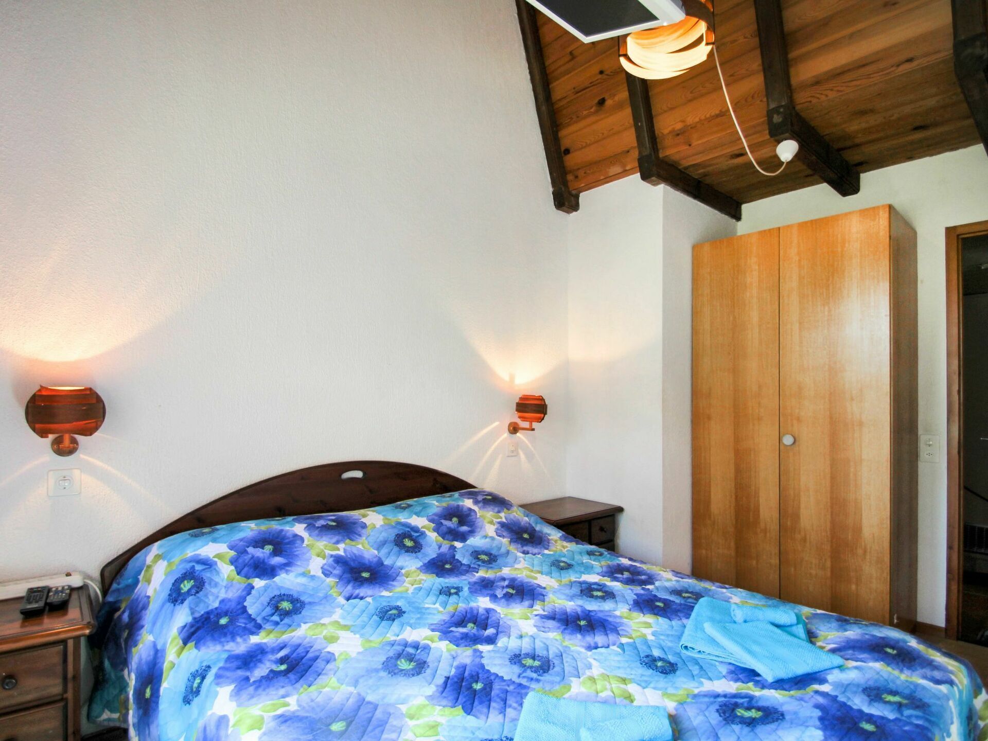 Une chambre à coucher avec un lit, une tête de lit en bois, deux lampes fixées au mur et une armoire.