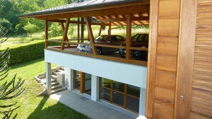 Une maison en bois à deux étages, dotée d’un balcon donnant sur un paysage verdoyant et luxuriant.