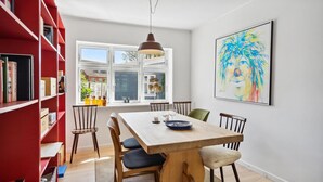 Een eetgedeelte met een houten tafel, stoelen en een rode boekenkast.