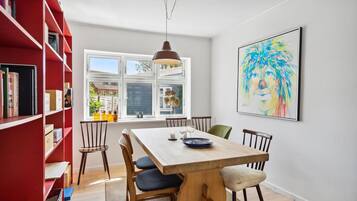 A dining area with a wooden table, chairs, and a red bookshelf.