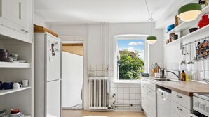 Een moderne keuken met witte kasten, een raam met uitzicht op groen en een radiator.