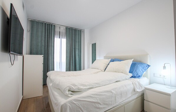 A bedroom with a bed, a nightstand, a TV mounted on the wall, and a window with curtains. - Beach front home in Los Alcázares (Los Alcázares)