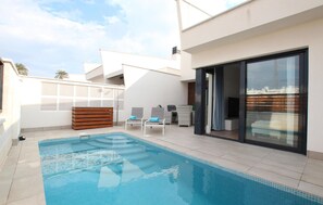 Een modern buitenzwembad met helderblauw water, ligbedden en een houten terras.