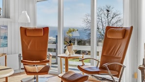 Ein modernes Zimmer mit zwei Ledersesseln, einem kleinen Tisch und Meerblick durch große Fenster.