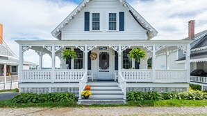 A white house with a porch, a front door, and a small garden with a pumpkin and flowers. - Quintessential seaside cottage in beautiful Pott's Point (Harpswell)