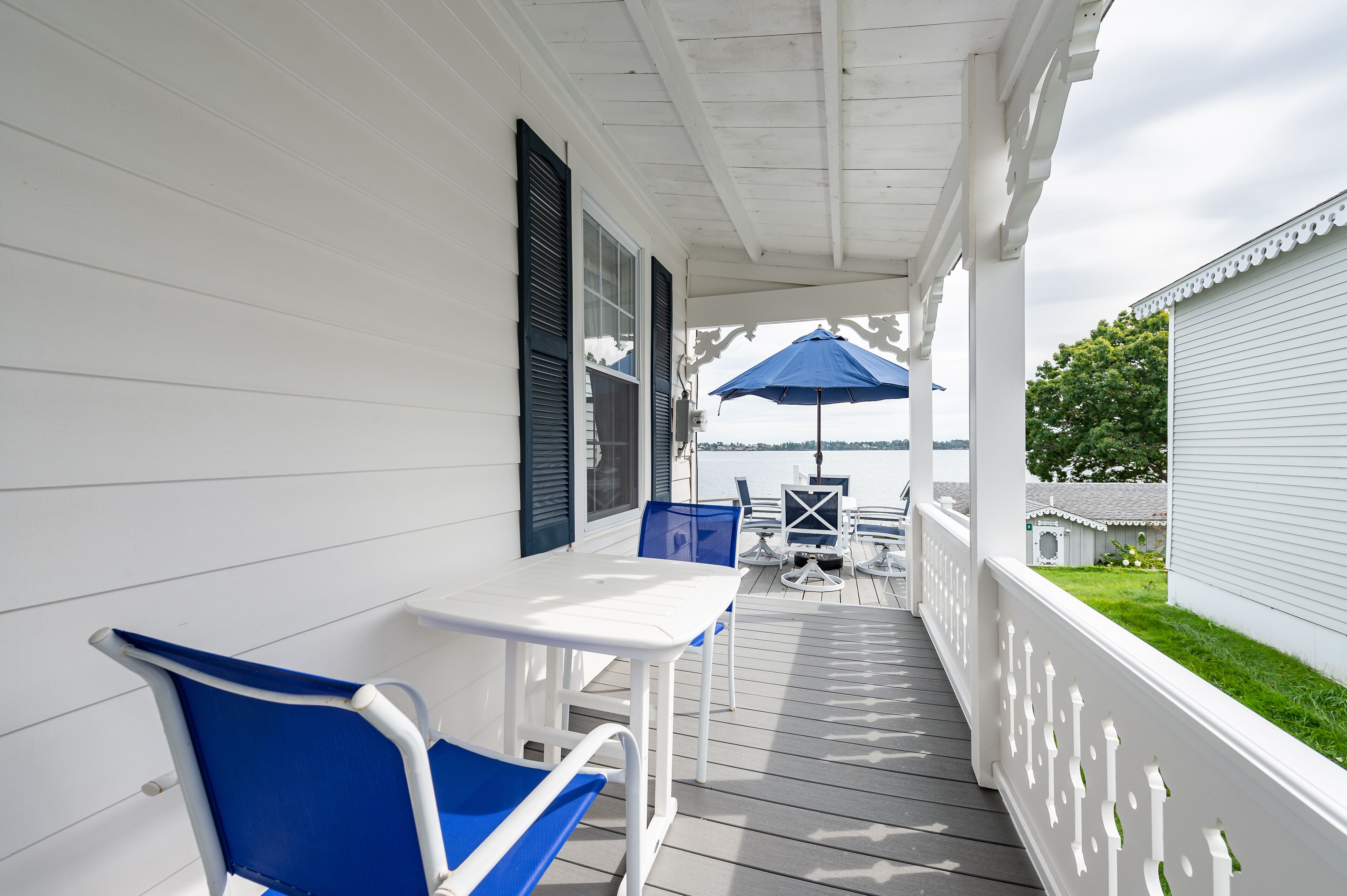 A covered porch with a white railing, a table, and blue chairs.
