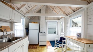 A compact kitchen with white cabinets, a wooden countertop, a sink, a stove, and a window offering a view of the sea. - Quintessential seaside cottage in beautiful Pott's Point (Harpswell)