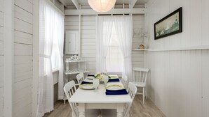 A dining area with a white table set for four, white chairs, and a hanging light fixture. - Quintessential seaside cottage in beautiful Pott's Point (Harpswell)