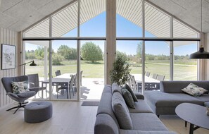 A spacious living area with a large glass door leading to an outdoor patio. Inside, there is a grey sofa, a matching ottoman, and a dining table with chairs. - Lovely home in Idestrup with WiFi (Idestrup)